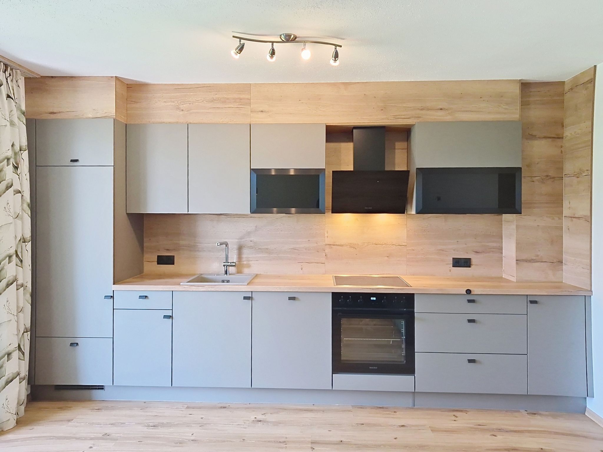 A modern kitchen with built-in appliances, a central island, and a wooden backsplash.