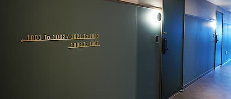 Un pasillo con puertas que tienen números de habitación y una lámpara sobre una de ellas.