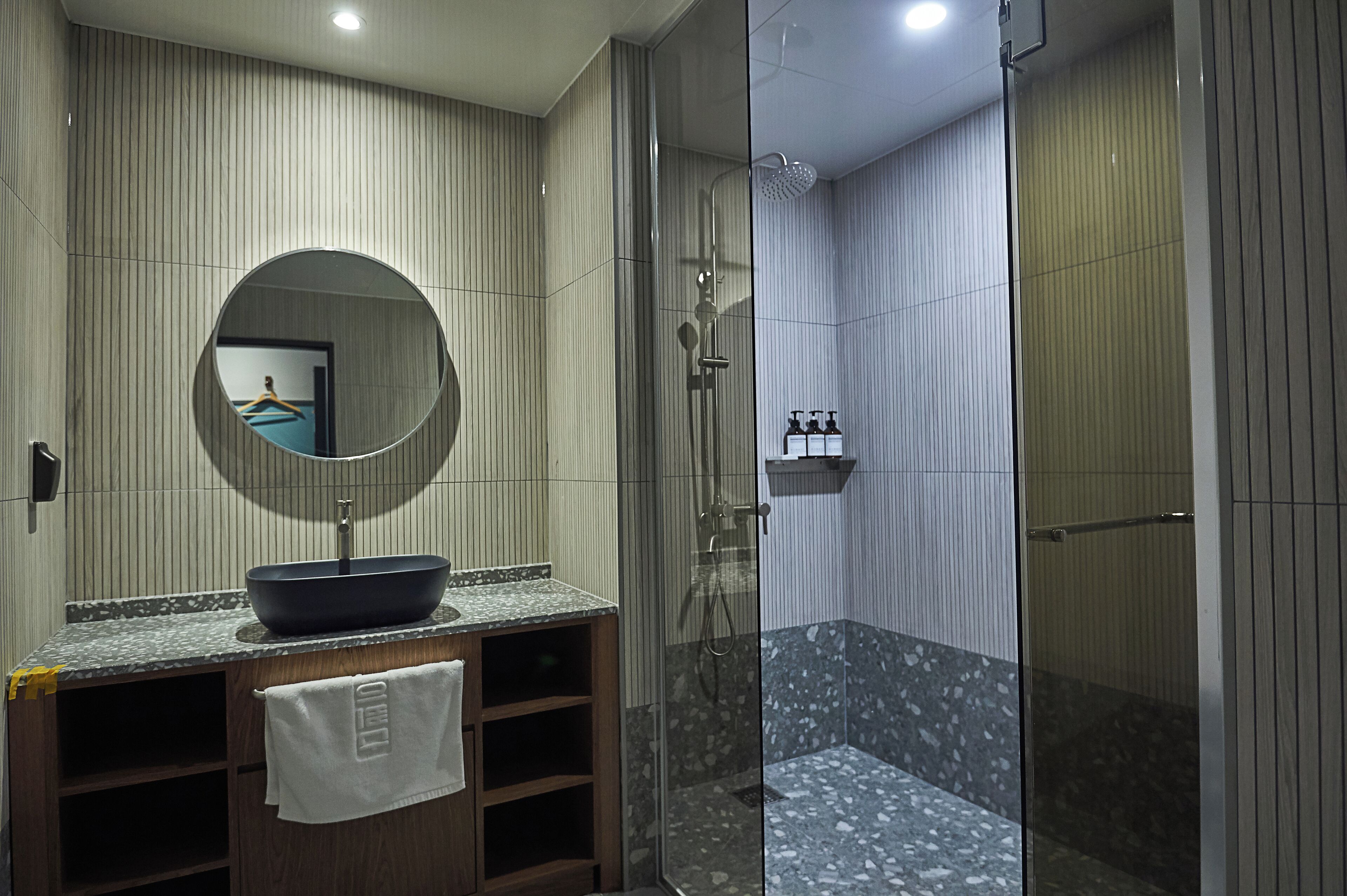 Uma casa de banho moderna com um espelho redondo, lavatório suspenso, cabine de duche com portas de vidro e chão de mosaico de mármore.
