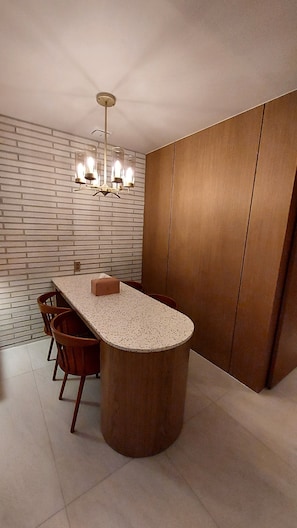 A modern dining area with a central island table, wooden panel walls, and a brick-patterned wall.