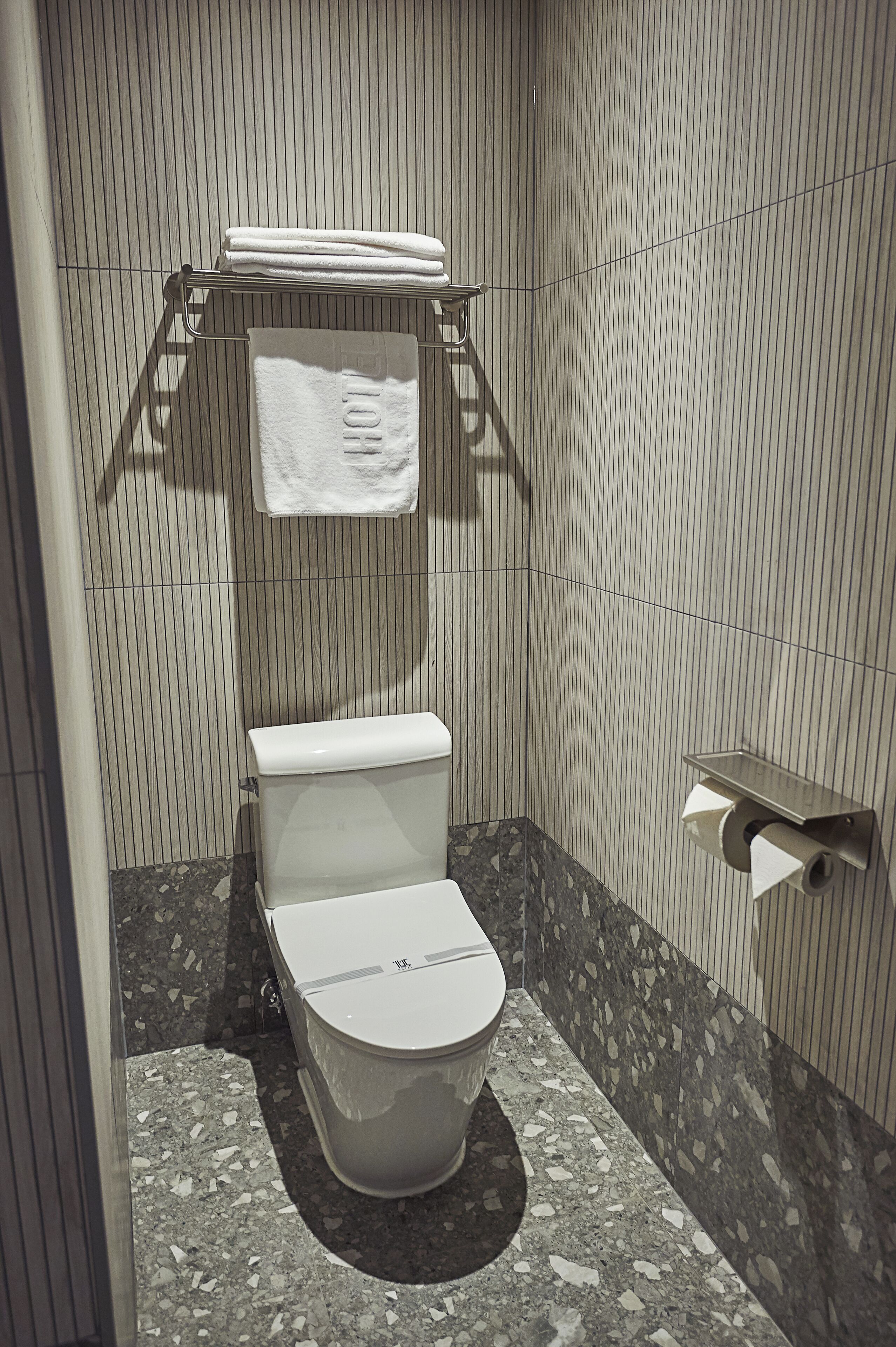A bathroom with a toilet, a towel rack with a towel, a toilet paper holder, and a marble floor.