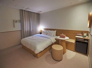 Habitació d'hotel amb llit, taula de nit, làmpada i una petita zona de cuina.