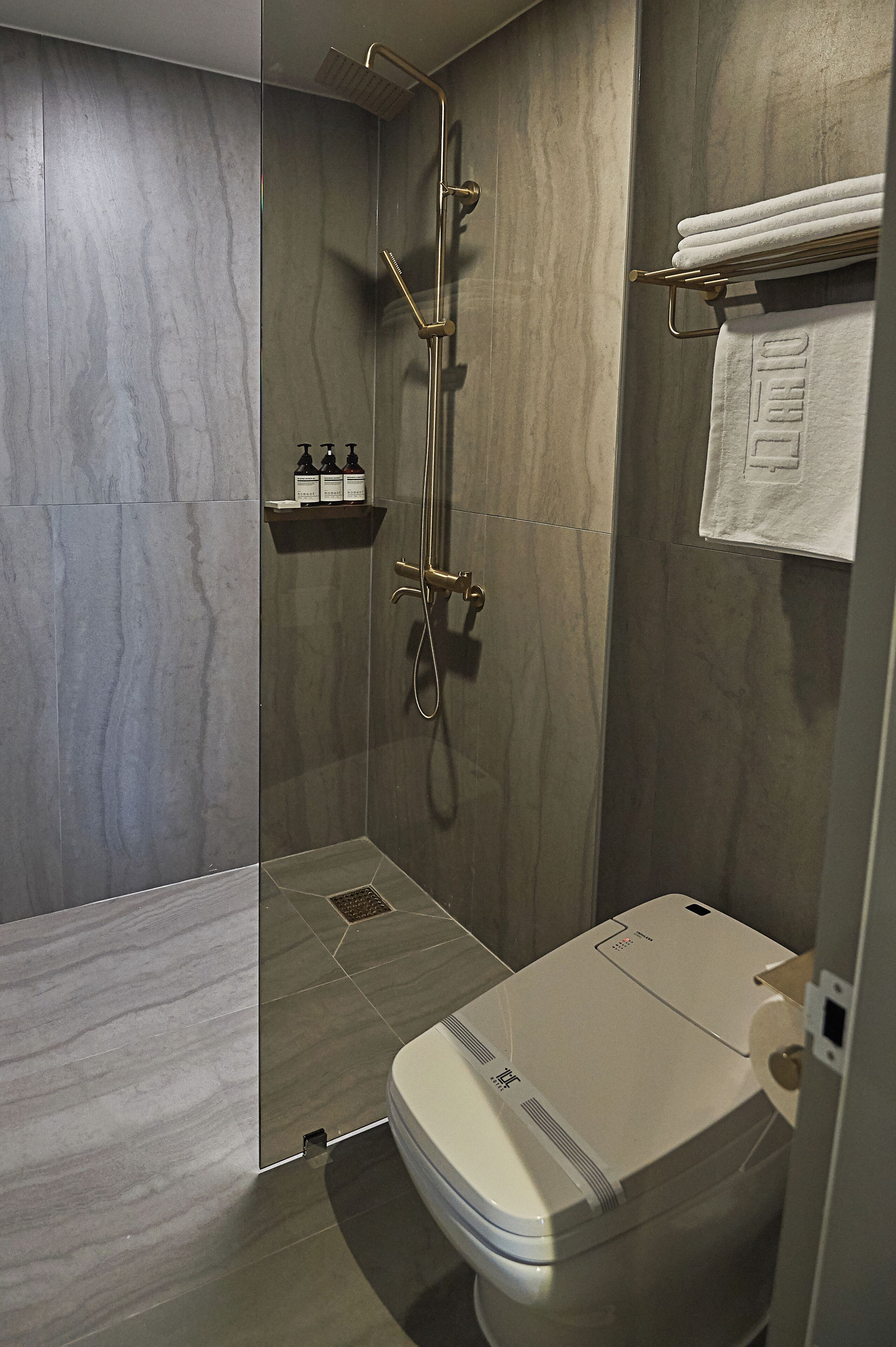 A modern bathroom with a glass-enclosed shower, a toilet, and a towel rack with a folded towel.