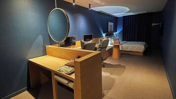 A modern hotel room with a wooden desk, a large round mirror, a bed with a headboard, and a wall-mounted television.
