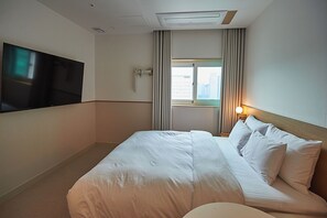 Habitació d'hotel amb un llit gran, televisió de pantalla plana penjada a la paret, finestra amb cortines i una làmpada de nit.