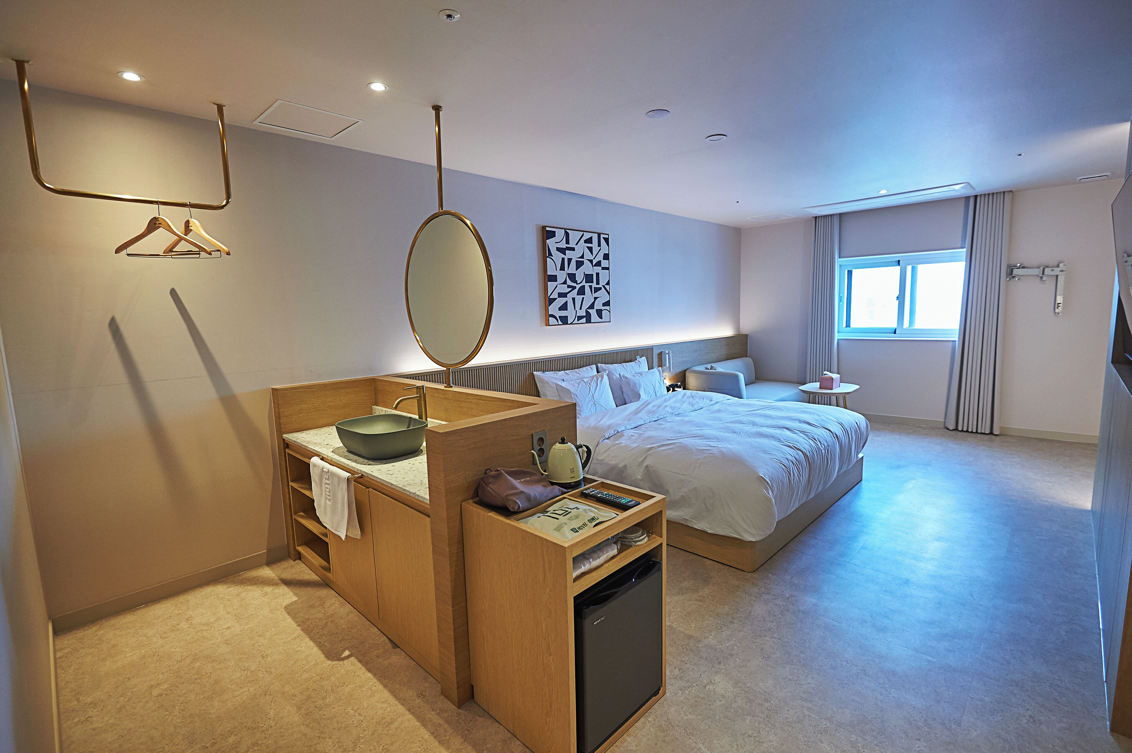 A hotel room with a wooden desk, a bed, a window, and a wall-mounted artwork.