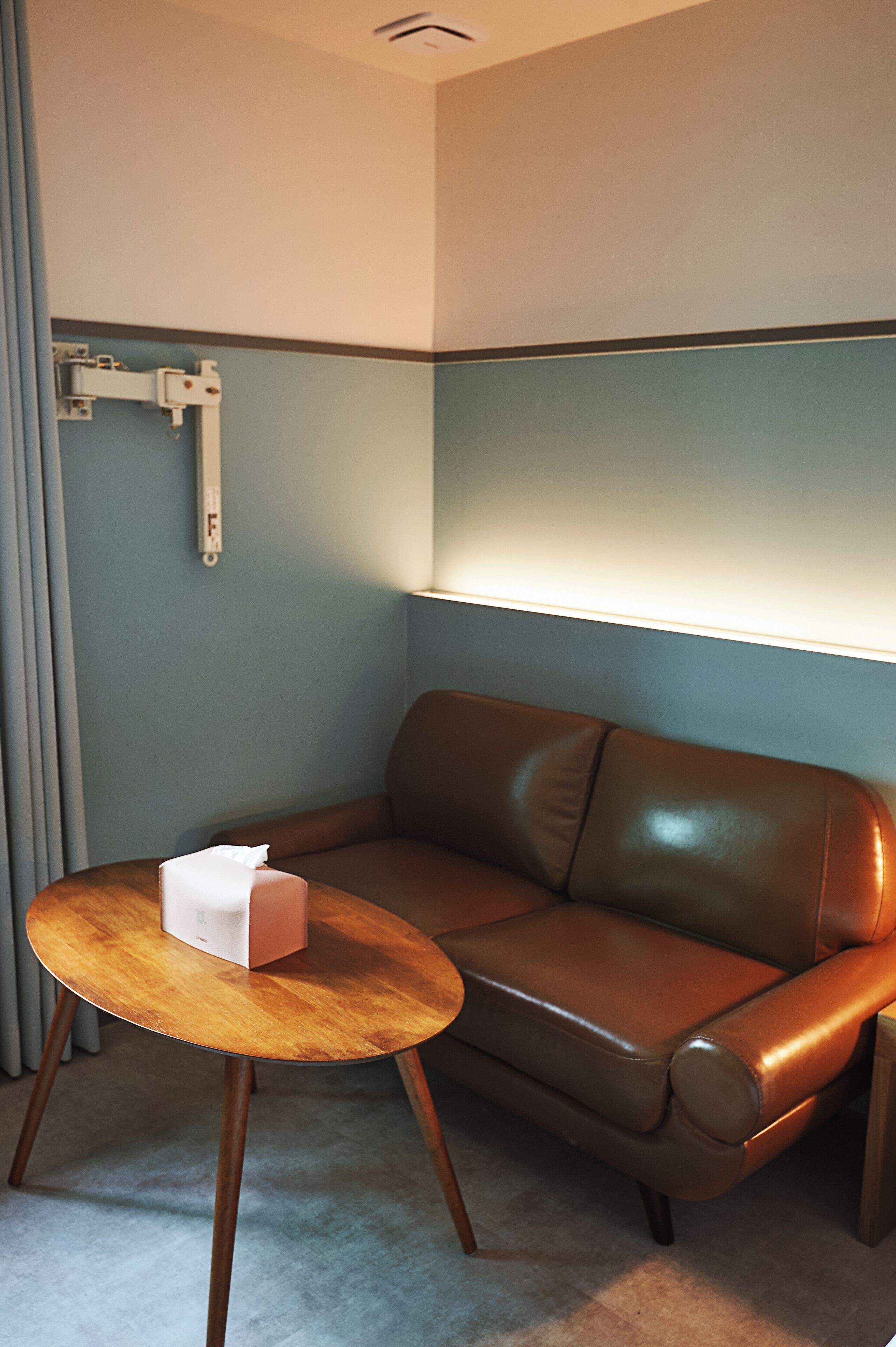 Een kamer met een bruine leren bank, een klein houten tafeltje met een zakdoos, en een lamp aan de muur.