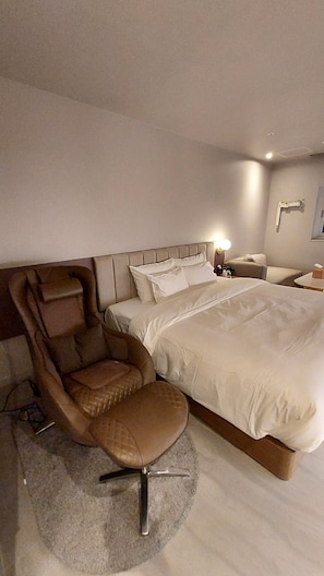 A modern hotel room with a large bed, a leather armchair, and a bedside table with a lamp.