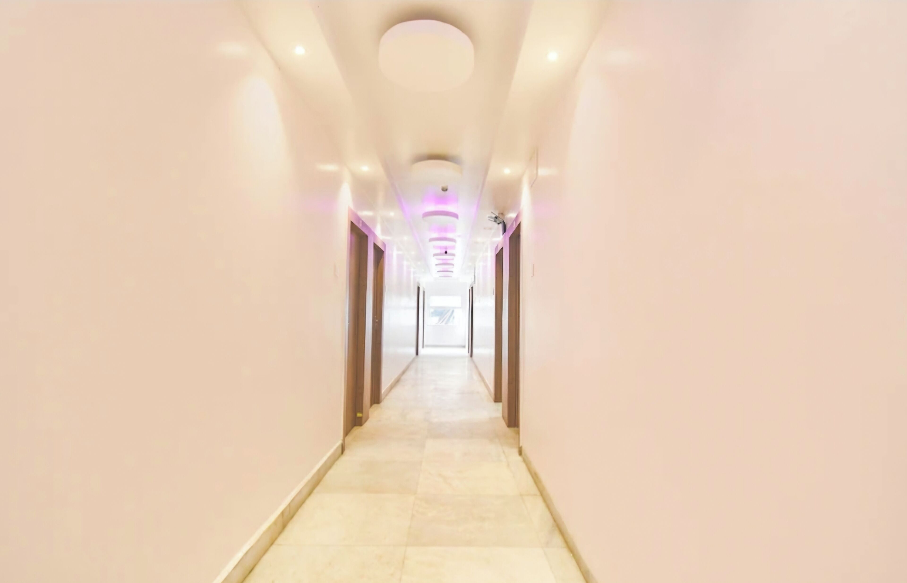 A long, narrow hallway with a light-colored floor and walls, leading to a bright room at the end.