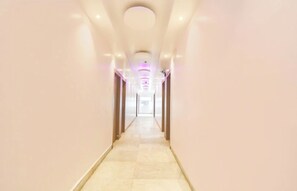 A long, narrow hallway with a light-colored floor and walls, leading to a bright room at the end.
