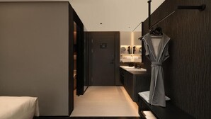 Una habitación de hotel moderna con una cama, un tocador con espejo y una bata colgada en un perchero.