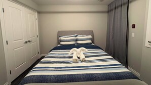 A bedroom with a bed, a headboard, a window with curtains, a door, and a light fixture. - Central | World's Largest Dino & Splash Park 🌟 (Drumheller)