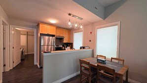 A kitchen with wooden cabinets, a stainless steel refrigerator, and a dining area with a table and chairs. - Central | World's Largest Dino & Splash Park 🌟 (Drumheller)