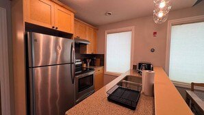 A kitchen with stainless steel appliances, wooden cabinets, granite countertops, a built-in oven, and a window with blinds. - Central | World's Largest Dino & Splash Park 🌟 (Drumheller)