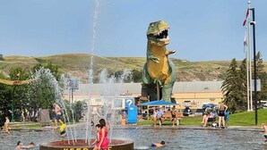 A public water fountain with a dinosaur statue, surrounded by people enjoying the water. - Central | World's Largest Dino & Splash Park 🌟 (Drumheller)