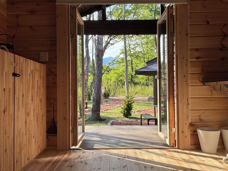 A wooden cabin interior with a view of a landscaped garden and a bench.