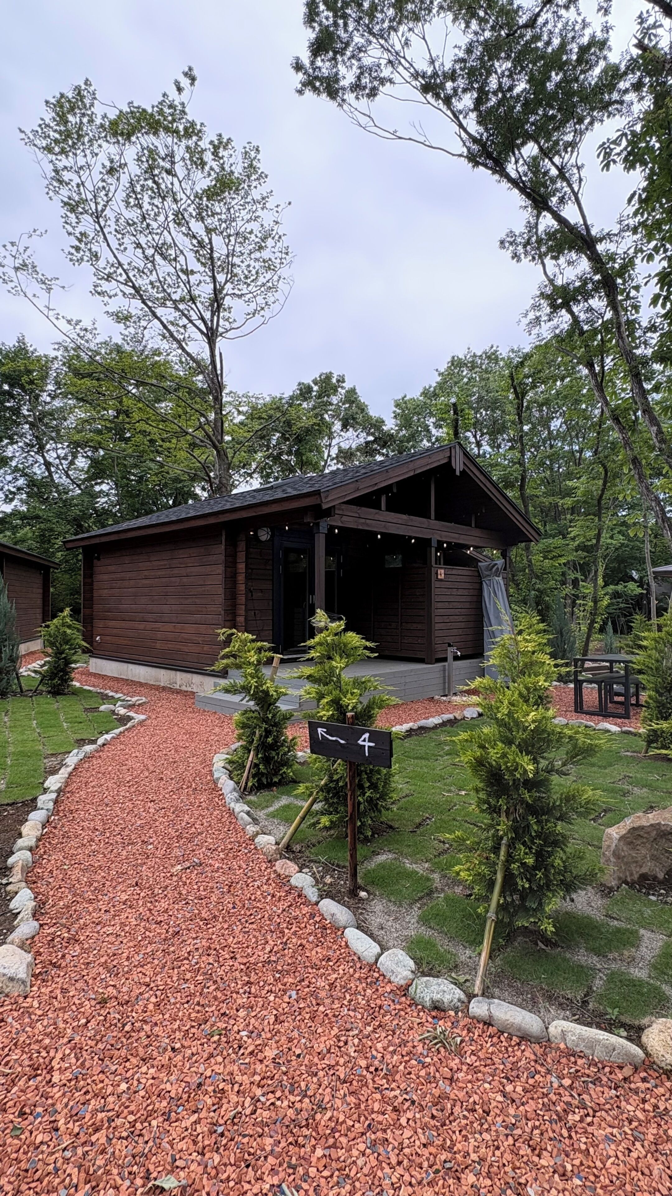 A wooden cabin with a gravel path leading to it, surrounded by trees and a small garden.