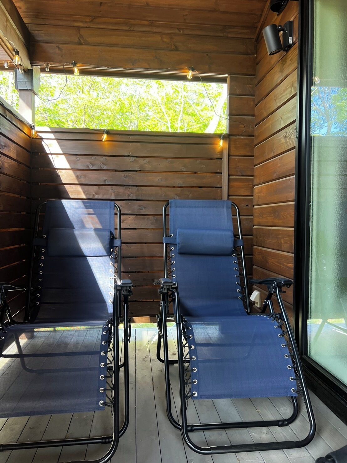 A room with two reclining chairs, wooden walls, a window, and a ceiling light fixture.