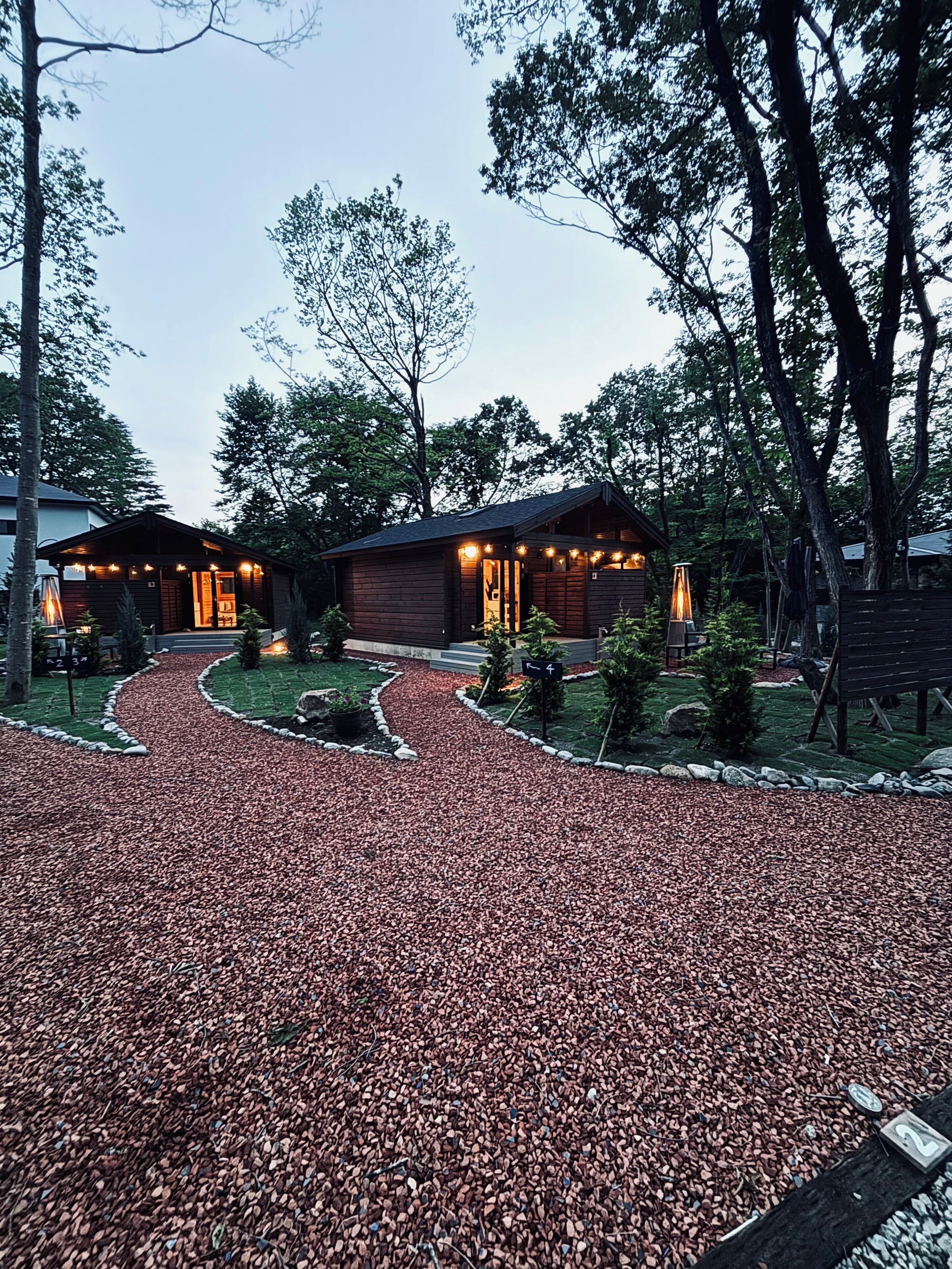 A wooden cabin with a gravel driveway, surrounded by trees.