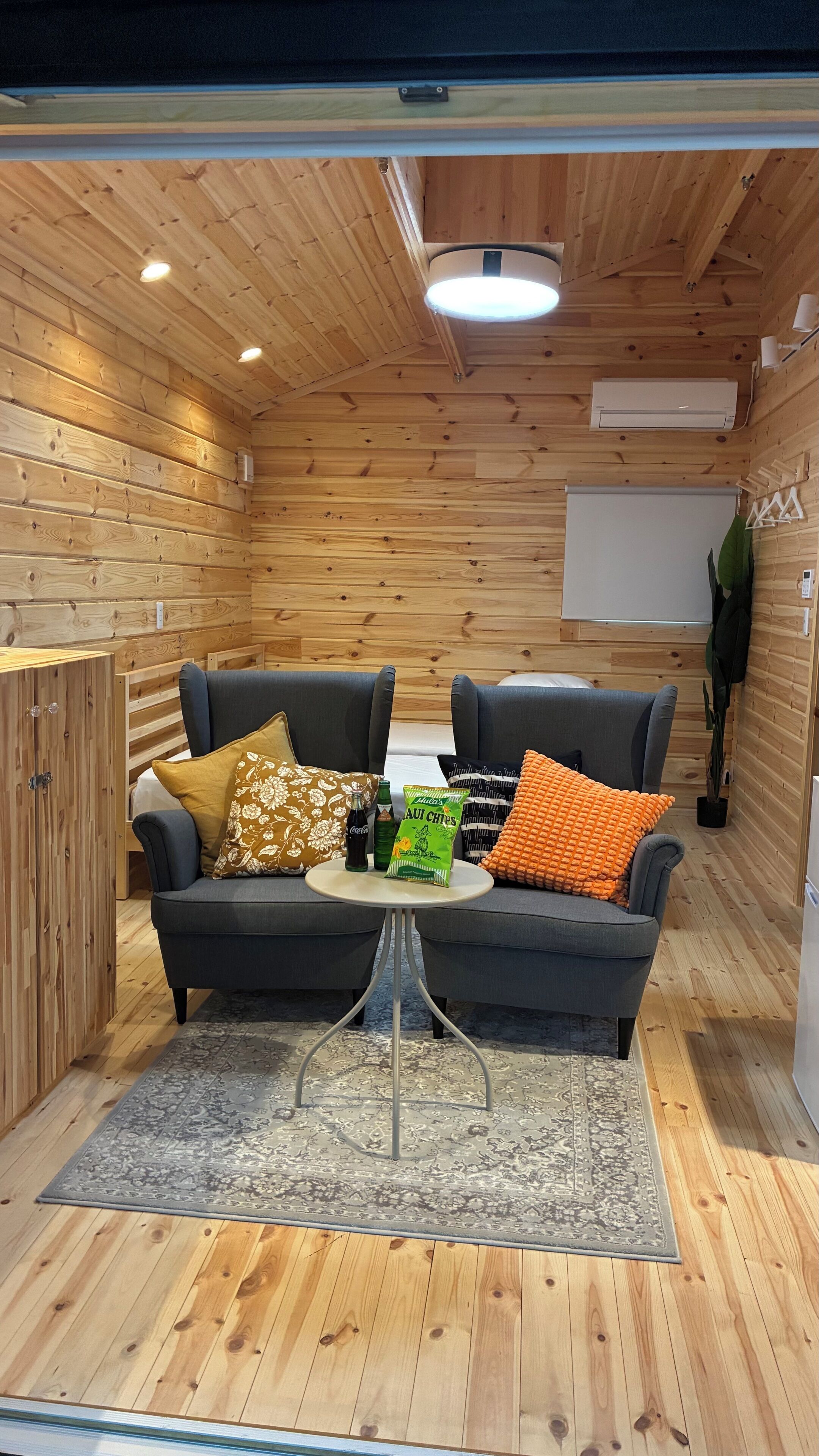 Una habitación acogedora con paredes y techo de madera, dos sofás oscuros, una mesita redonda y una planta en maceta.