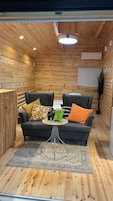 A cozy room with wooden walls and ceiling, two dark sofas, a small round table, and a potted plant.