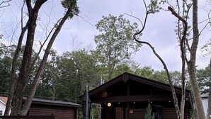 A rustic cabin with a porch, surrounded by trees and a gravel path.