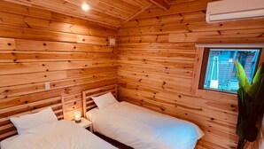 A wooden cabin room with two beds, a window, and a nightstand with a lamp.