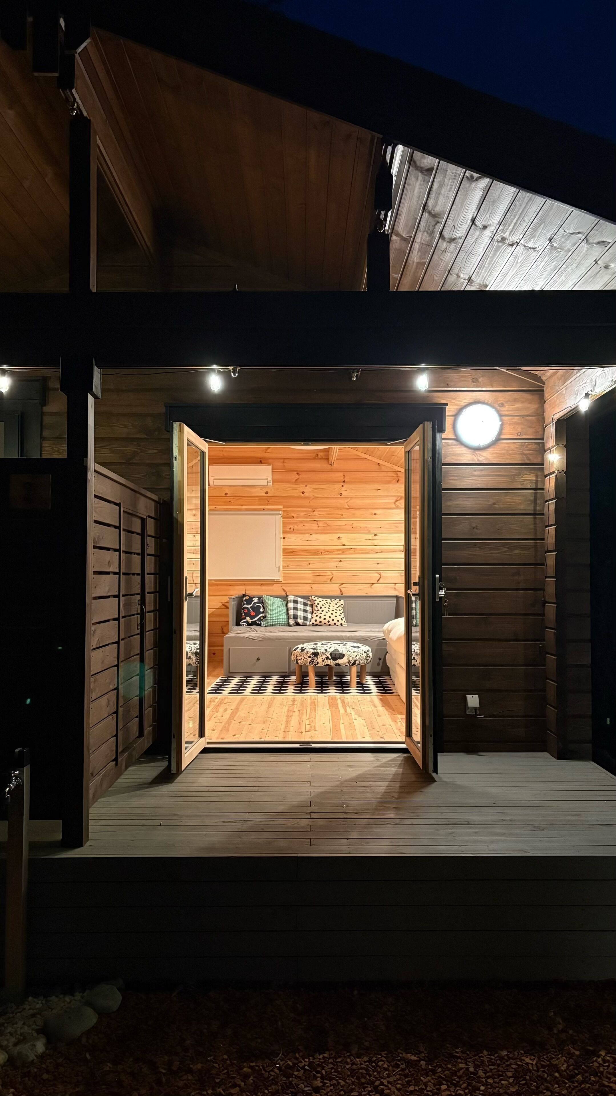 Una cabaña de madera con un amplio umbral abierto que da a una habitación con una cama y almohadas.