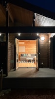 Eine Holzhütte mit großem, offenem Durchgang zu einem Zimmer, das ein Bett und Kissen zeigt.