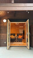 Uma porta deslizante aberta dá acesso a uma sala com dois sofás, uma mesinha e uma janela com vista.