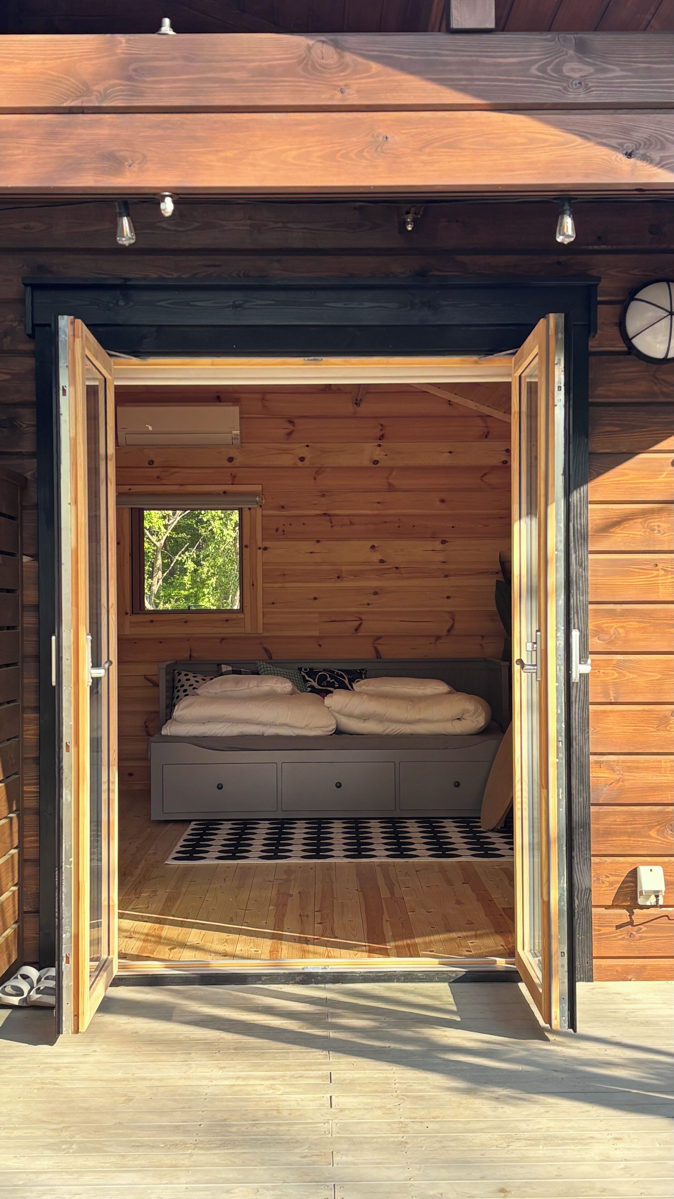 A wooden cabin with a bed, a window, and a door.