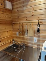 Una cocina con paneles de madera, un lavamanos de acero inoxidable y varios utensilios colgados en la pared.