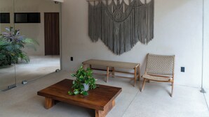 Ein Zimmer mit Holztisch, gewebtem Sessel, einer Bank und einer Wanddekoration aus Makramee.