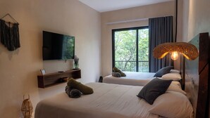 Ein modernes Hotelzimmer mit zwei Betten, einem Flachbildfernseher, einem großen Fenster mit Vorhängen und einer ungewöhnlichen gewebten Leuchte.