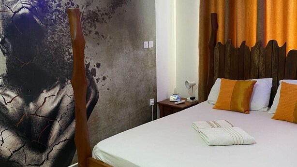 Una habitación de hotel con una cama grande, aire acondicionado de pared, una mesita de noche con lámpara y una cortina.