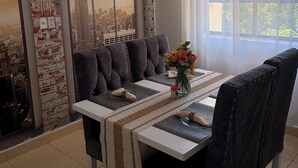 Comedor con una mesa preparada para cuatro, un florero con flores y un mural de paisaje urbano en la pared.