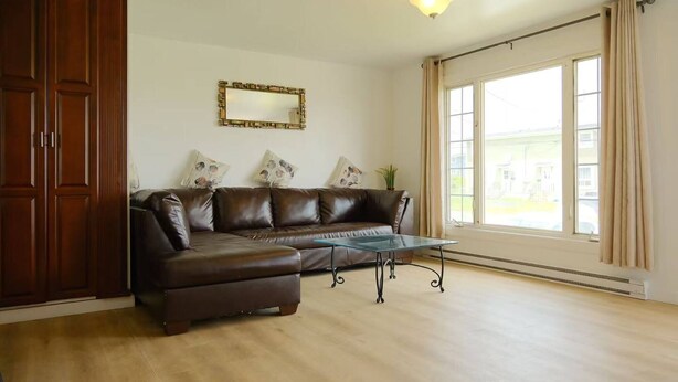 A living room with a brown leather sofa, a glass coffee table, a wooden wardrobe, and a large window with curtains. - Warm and Bright 3 Bedroom Detached House·sydney (Sydney)