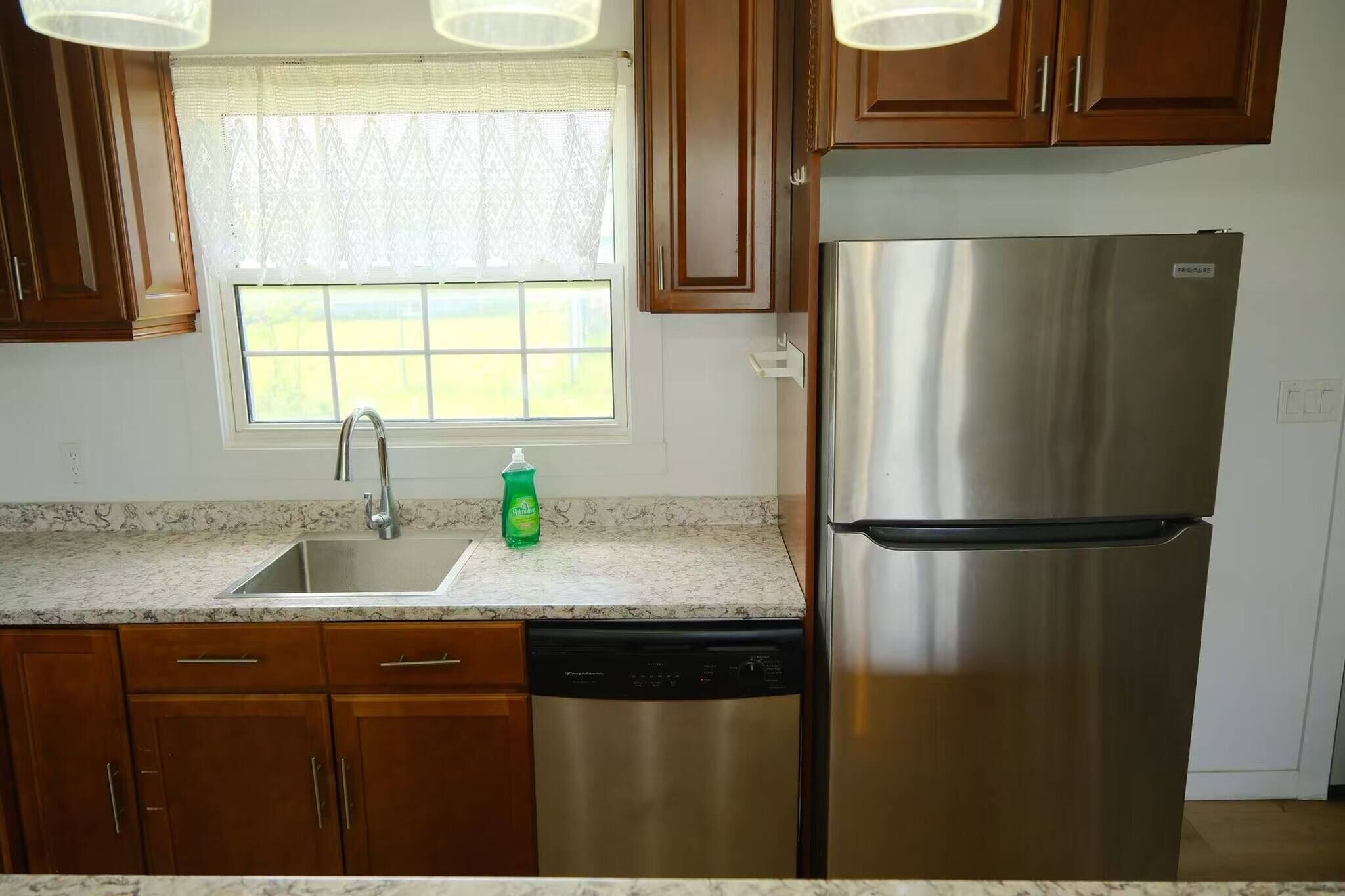 A kitchen with wooden cabinets, a stainless steel refrigerator, a dishwasher, and a window with a view.