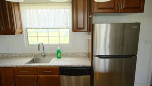 A kitchen with wooden cabinets, a stainless steel refrigerator, a dishwasher, and a window with a view. - Warm and Bright 3 Bedroom Detached House·sydney (Sydney)