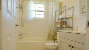 A bathroom with a bathtub, toilet, and shelves with towels. - Warm and Bright 3 Bedroom Detached House·sydney (Sydney)