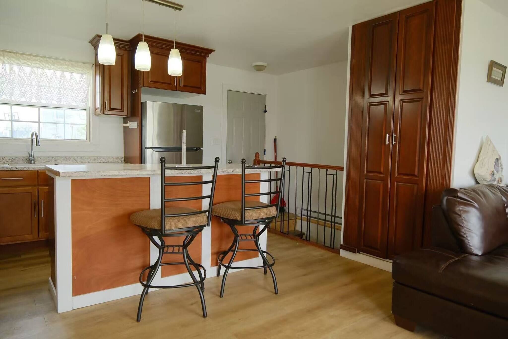 Una cocina con una isla central, dos taburetes de bar, un refrigerador y armarios de madera.