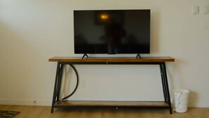 A television mounted on a wooden stand with a metal frame, positioned against a plain wall.