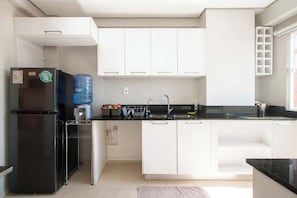 Eine moderne Küche mit weißen Schränken, einem schwarzen Kühlschrank, einem Wasserspender und einem Waschbecken.