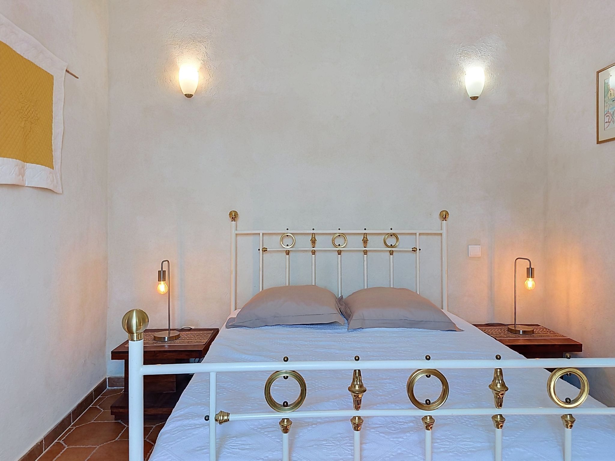 Un letto con struttura in metallo bianco e dettagli in ottone, due comodini e luci fissate alla parete.