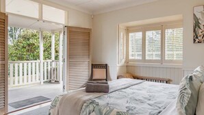 A bedroom with a bed, a window with shutters, a door leading to an outdoor area, and a view of greenery.