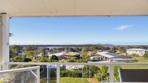 Un balcone con vista su una zona residenziale, un corpo d'acqua e montagne lontane.