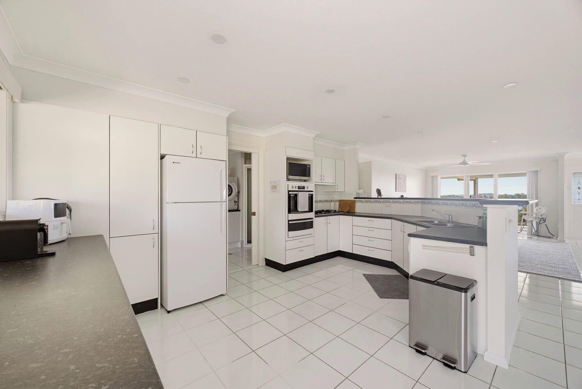 A modern kitchen with white cabinetry, a built-in oven, and a stainless steel trash bin.