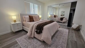 Ein Schlafzimmer mit einem Bett, Nachttischen, einem Spiegel und einem Kleiderschrank.