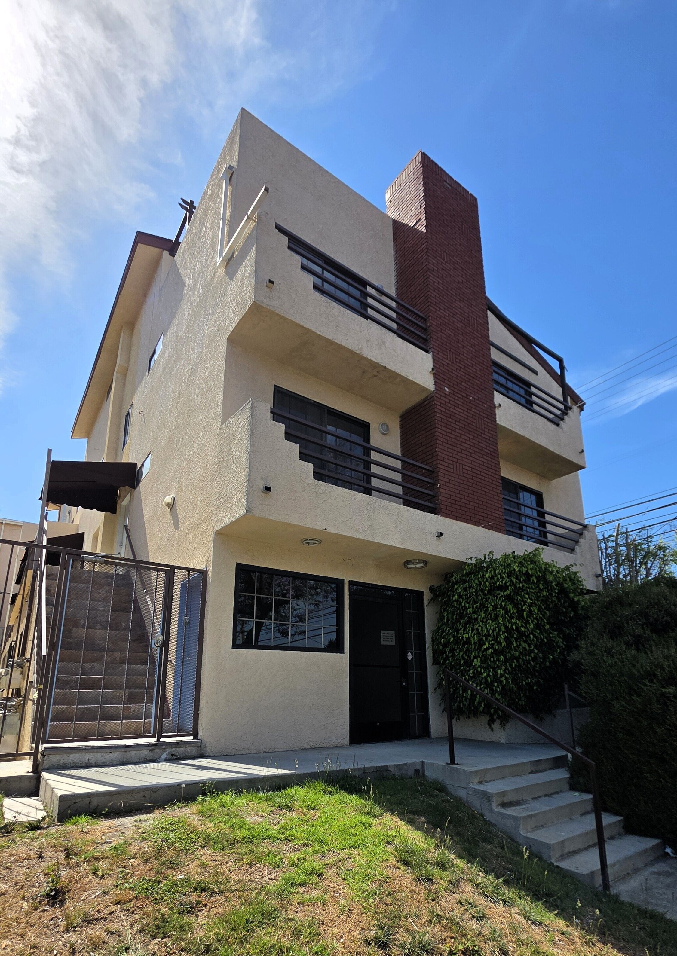Un edificio de varios pisos con una chimenea de ladrillo, una entrada con portón y un pequeño jardín delantero con escalones que conducen a la puerta.