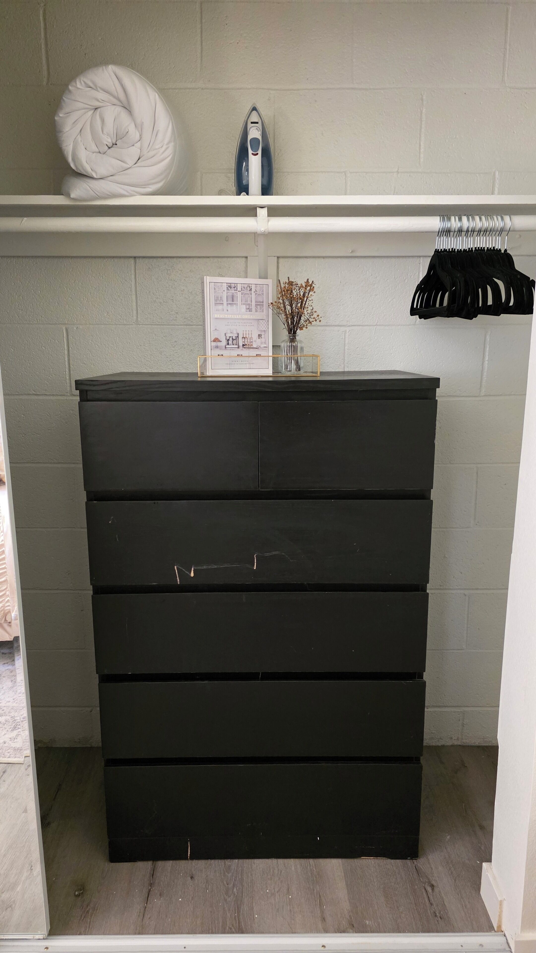 Un meuble de rangement noir sur lequel sont posés un linge blanc et un fer à repasser bleu.